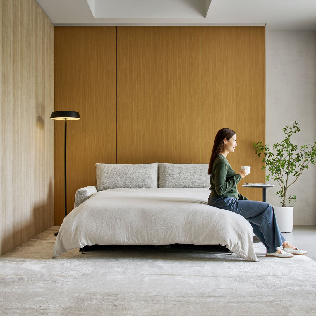 Woman with a coffee sitting on the opened Nadia Sofa Bed