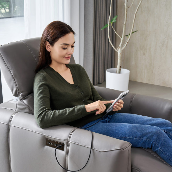 Woman reclined in the Bailey 1 Seat Armchair, charging a tablet from the side panel