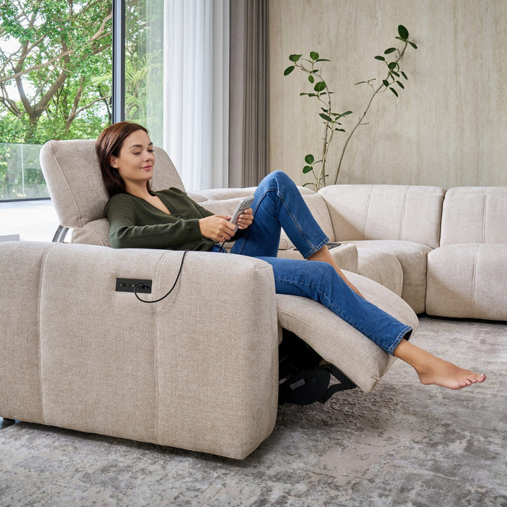 Woman reclined on a Bailey corner seat, charging her phone from the side panel