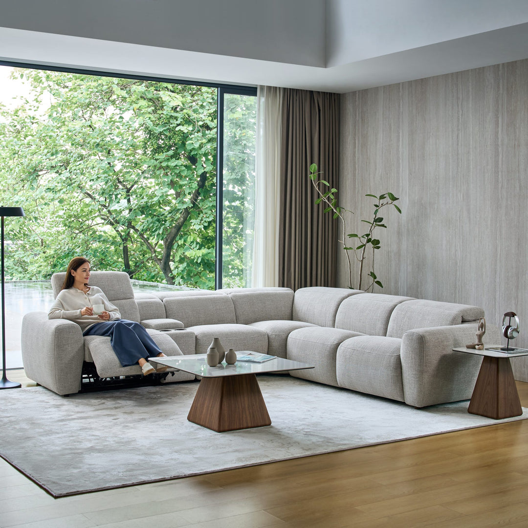 Woman relaxing on a reclined seat of the Cambridge corner sofa in light grey fabric