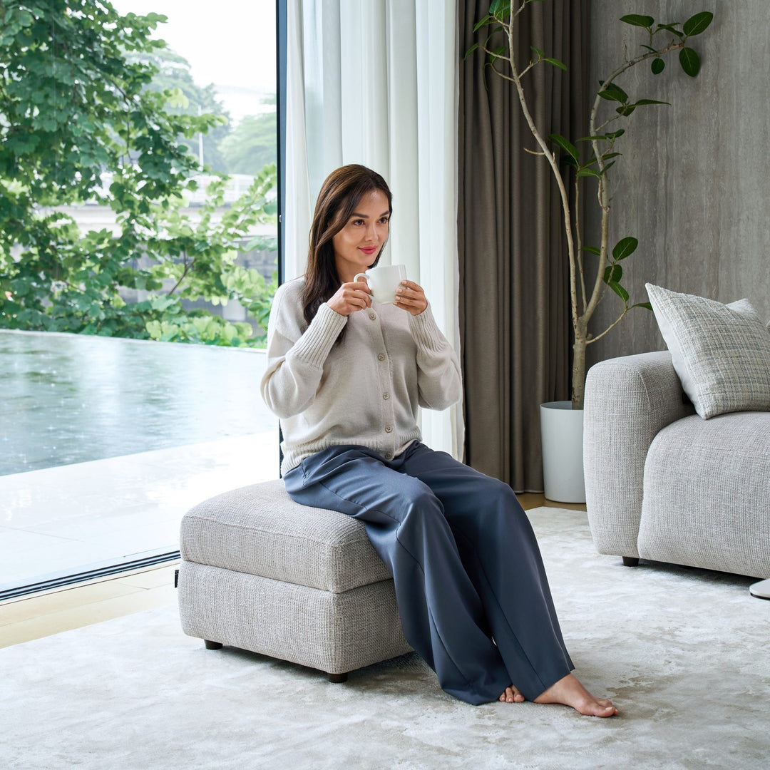 Woman seated on the Cambridge storage footstool in light grey fabric