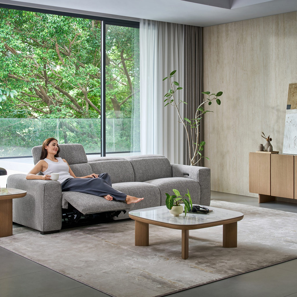 Woman stretched out on a reclined seat of the Jeddah 3 seat sofa in grey fabric