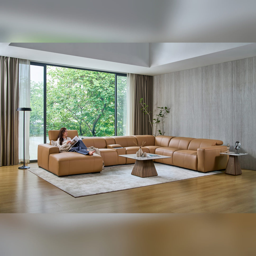 Woman reading on the chaise of the Jeddah U-shape sofa in tan leather
