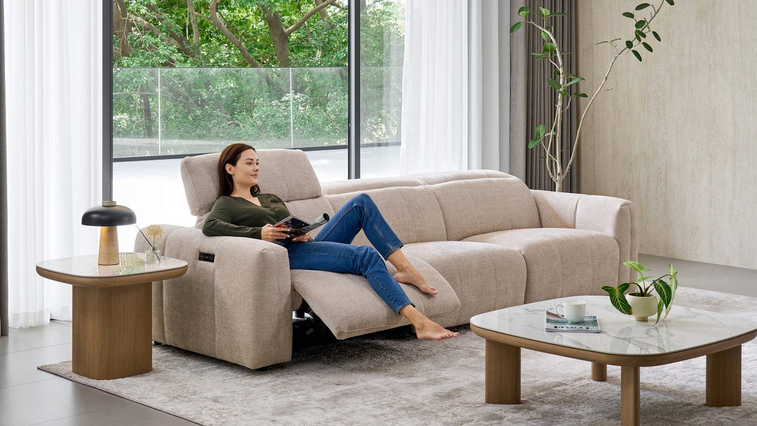 Woman relaxing on the Bailey 3 Seat Sofa in beige fabric beside timber side and coffee tables